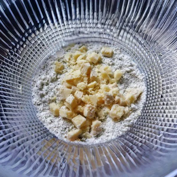 Potong kecil 30 gr mentega, lalu masukkan ke dalam campuran tepung. Remas-remas menggunakan jari sampai bertekstur seperti pasir kasar. Masukkan 35 gr keju parut, aduk rata.