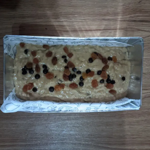 Tuang adonan kedalam loyang.  Beri topping raisin dan chococip diatasnya.
