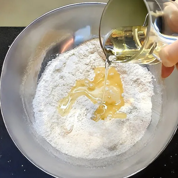 Masukkan tepung almond, aduk kembali hingga semua bahan kering tercampur rata. Tuangkan minyak jagung ke dalam campuran tepung, aduk rata dengan spatula hingga menjadi adonan.