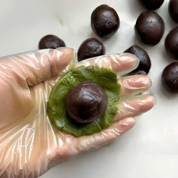 Ambil satu bulatan adonan matcha, pipihkan di telapak tangan. Letakkan satu bulatan adonan cokelat di tengah, lalu bungkus dengan adonan matcha dan bulatkan kembali.