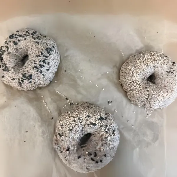 Buat lubang besar di tengahnya, rapikan sisi sekeliling hingga berbentuk bagel. Olesi permukaan dengan sedikit air, lalu taburi campuran 5 gr biji wijen hitam dan 5 gr biji wijen putih.