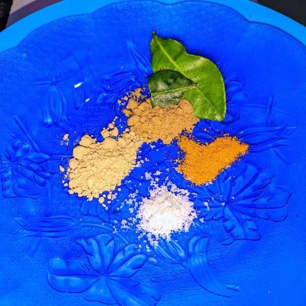 Campurkan kunyit bubuk, bawang putih bubuk, lada bubuk, daun jeruk, ketumbar bubuk, garam, dan air untuk membuat bumbu marinasi.