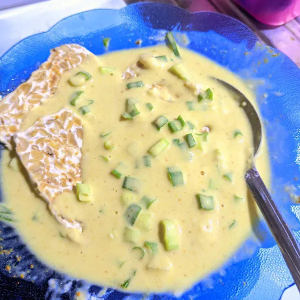 Masukkan potongan tempe ke dalam bumbu tepung, pastikan semua sisi terbalur rata.