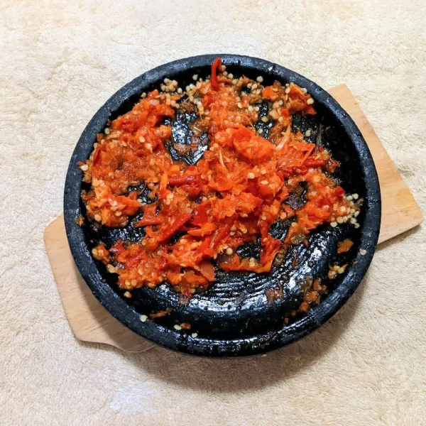 Haluskan cabai merah besar, cabai rawit, bawang putih, dan bawang merah dengan cobek.