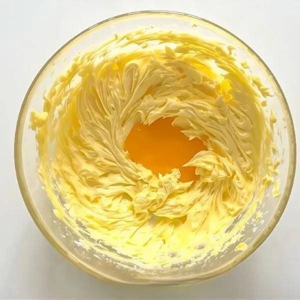 Tambahkan kuning telur secara bertahap, lalu kocok hingga rata dan lembut.