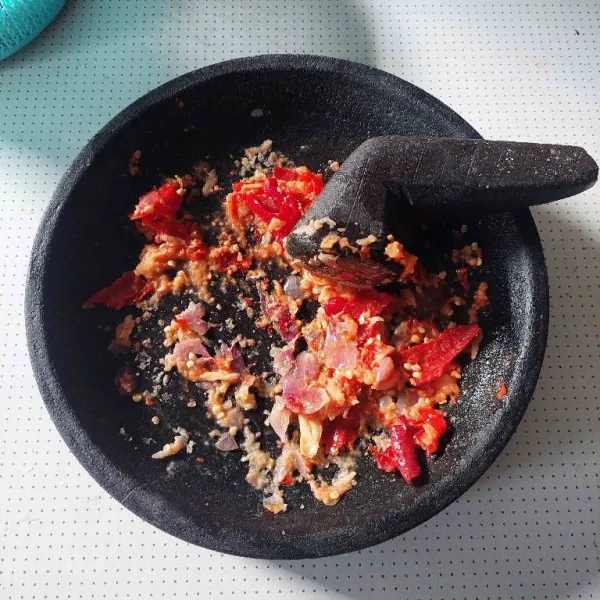 Haluskan cabe, bawang merah, bawang putih, dan kemiri menggunakan ulekan.