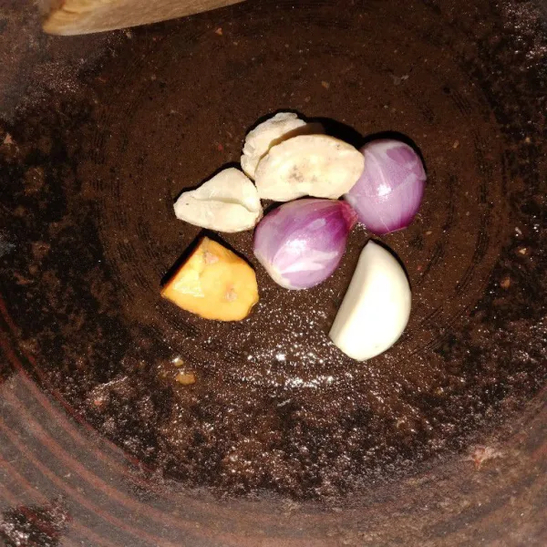 Haluskan bawang merah, bawang putih, kunyit, dan kemiri menggunakan ulekan.