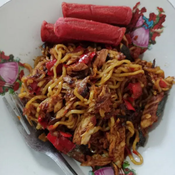 Jangan lupa untuk koreksi rasa. Jika sudah pas, matikan kompor dan pindahkan mie ke dalam piring, lalu beri topping potongan sosis.