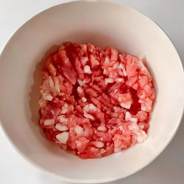 Masukkan daging babi cincang ke dalam mangkuk, lalu tambahkan air rendaman jahe dan daun bawang sedikit demi sedikit sambil diaduk.