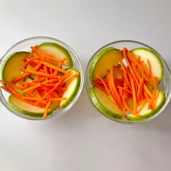 Siapkan mangkuk tahan panas, lalu lapisi sisi mangkuk dengan irisan zucchini tipis. Taburkan wortel iris tipis di dasar mangkuk.