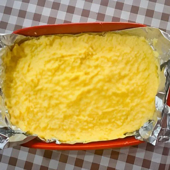 Haluskan 50 gr biskuit, lalu campur dengan 5 gr mentega cair. Ratakan di dasar wadah tahan panas sebagai lapisan bawah. Tuang adonan susu padat di atas lapisan biskuit. Ratakan