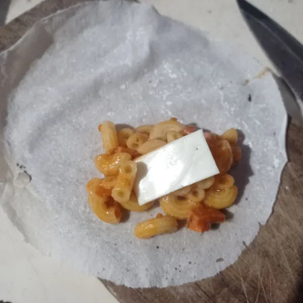 Ambil selembar kulit lumpia, beri isian makaroni dan irisan keju, lipat atas dan samping lalu gulung.