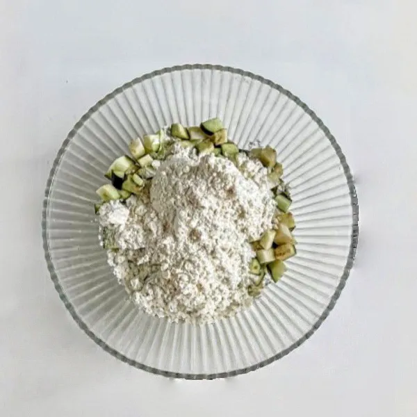 Campurkan terong dengan tepung terigu dan air. Aduk rata hingga menjadi adonan kental.