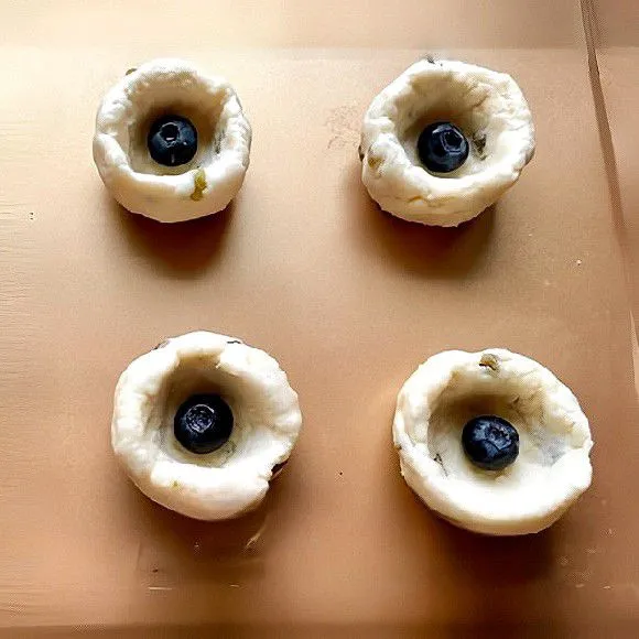 Gilas adonan, bentuk bulat, lalu pipihkan sedikit. Letakkan blueberry segar secukupnya di atas adonan