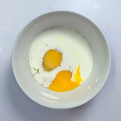 Pecahkan 2 butir telur ke dalam mangkuk. Tambahkan 80 ml susu cair, lalu kocok hingga tercampur rata