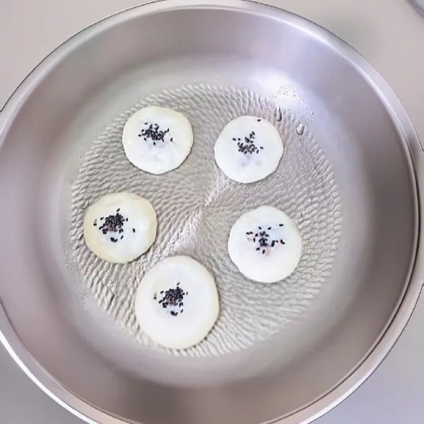 Taburkan wijen hitam di atas kue. Panggang kedua sisi hingga berwarna keemasan. Tambahkan sedikit air di tepi wajan, tutup, dan biarkan kukus sebentar selama ±1 menit