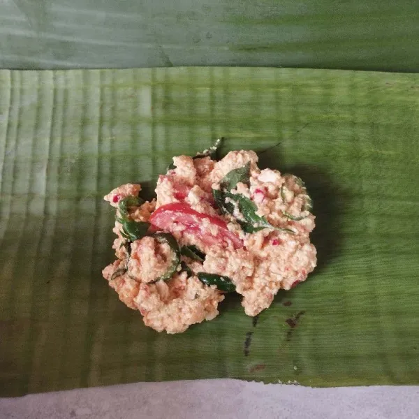 Ambil 2 sendok makan adonan pepes, lalu taruh di selembar daun pisang. Gulung dan semat dengan lidi.