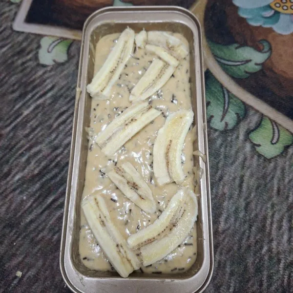 Olesin loyang dengan margarin secukupnya. Tuang adonan kedalam loyang lalu tambahkan irisan pisang sebagai toping