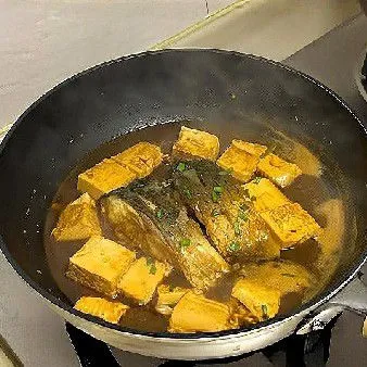 Tambahkan tahu berbentuk dadu, lanjutkan merebus selama 10 menit hingga kuah sedikit mengental. Taburi daun bawang cincang.