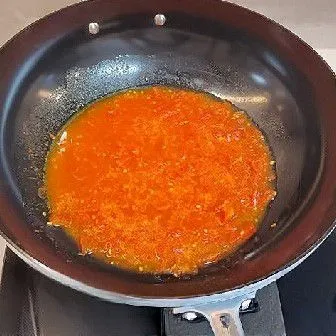 Panaskan minyak goreng di wajan, lalu masukkan tomat yang telah dipotong berbentuk dadu dan tumis hingga tomat mengeluarkan sari dan menjadi agak lembek.