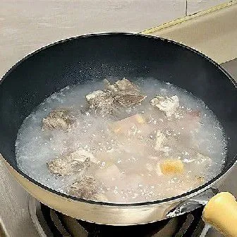 Tuang 800 ml air panas ke dalam wajan, masukkan tulang iga, rebus dengan api besar hingga mendidih, kemudian kecilkan api dan biarkan mendidih perlahan selama 20 menit