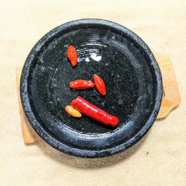 Haluskan cabe rawit dan cabe merah besar sebagai bumbu halus menggunakan ulekan.