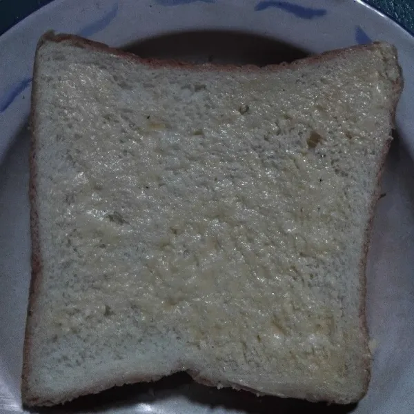 Oles salah satu sisi roti tawar dengan margarin.
