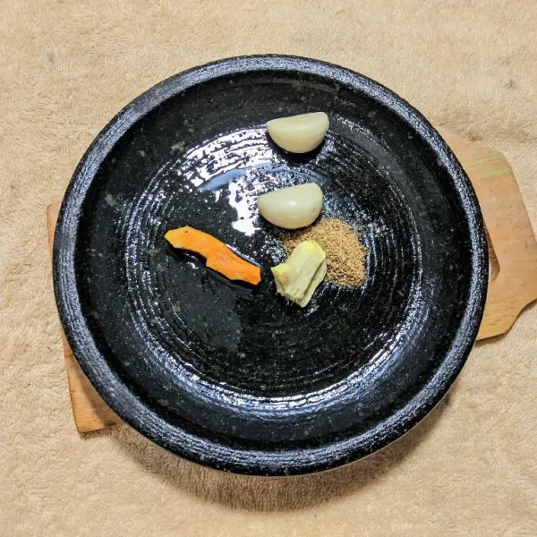 Haluskan bawang putih, kunyit, jahe, dan ketumbar bubuk menggunakan ulekan.