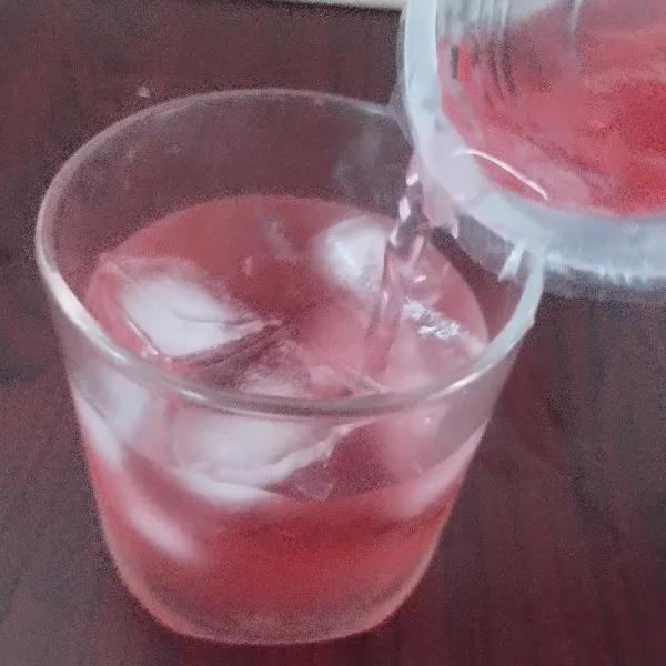 Dalam gelas saji, beri beberapa es batu, lalu tuangkan teh rosella ke gelas.