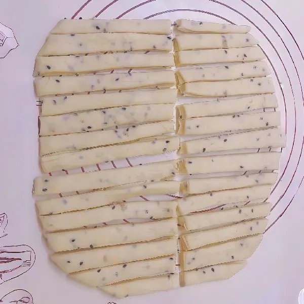 Potong lembaran adonan menjadi strip memanjang. Ambil satu strip, pegang kedua ujungnya, lalu puntir ke dua arah hingga membentuk twisted stick