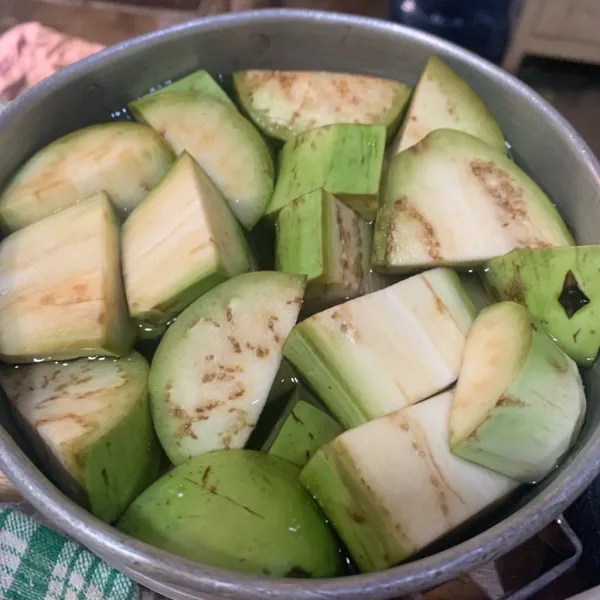 Iris terong dan rendam di air sembari menghaluskan bumbu