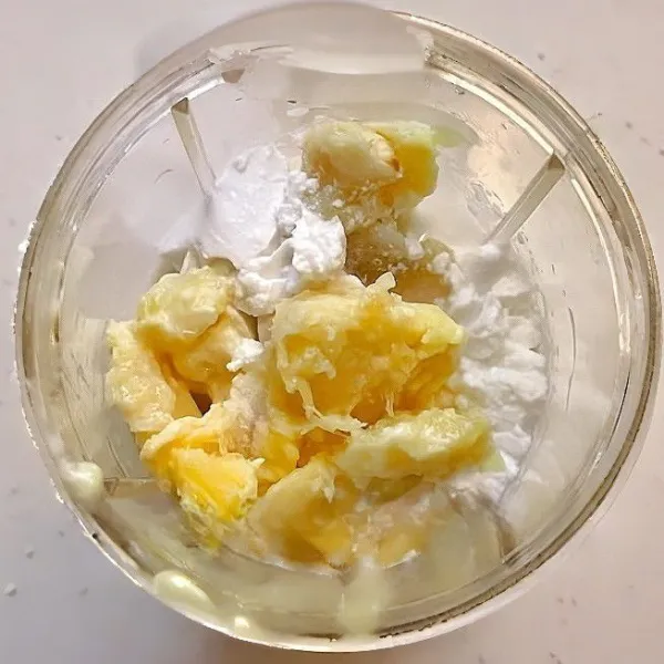 Masukkan 150 gr daging durian ke dalam blender. Tambahkan 65 ml santan kental dan 100 ml susu cair