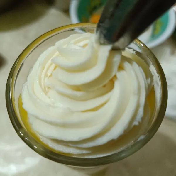 Mixer whipcream bubuk bersama air es hingga kamu, siapkan gelas saji, tuang jus mangga, lalu beri whipcream secukupnya