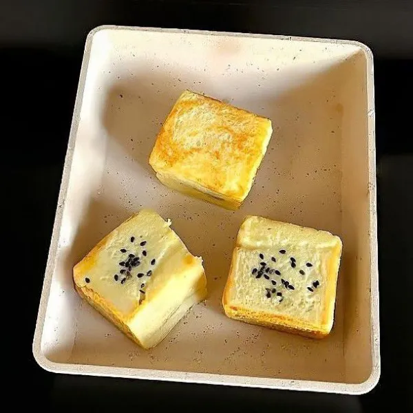Panaskan wajan dengan 5 gr mentega, masak roti dengan api kecil hingga kedua sisi berwarna keemasan. Tambahkan 2 gr wijen hitam di atasnya